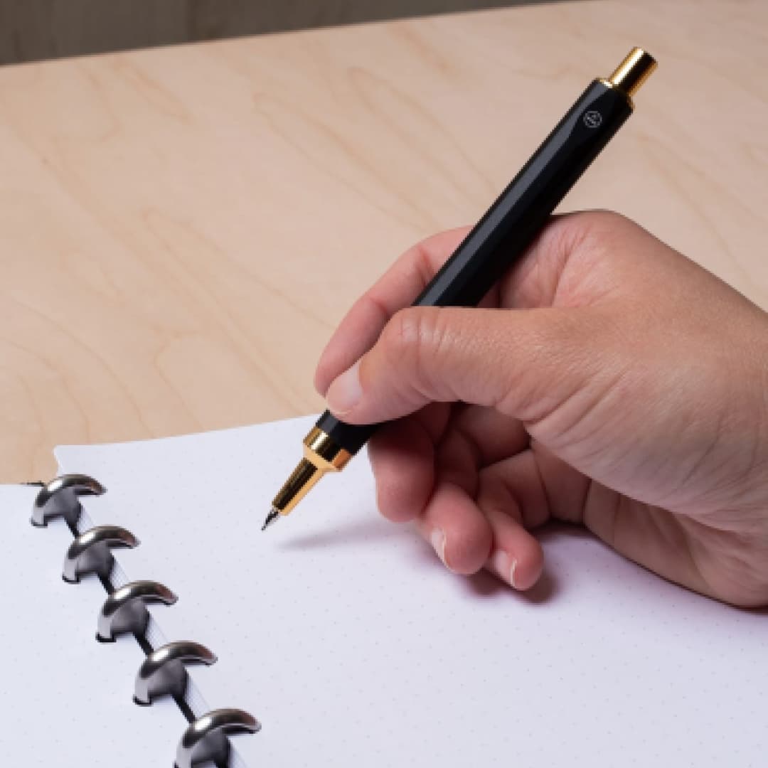 Hand holding black machined steel mechanical pencil with brass tip and top.